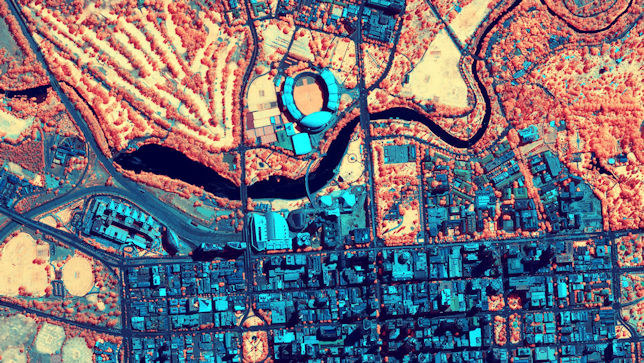 Luftaufnahme einer Stadt mit einem großen Stadion im Mittelpunkt, wobei die virtuelle Farbpalette aus Blau-, Rot- und Orangetönen besteht  