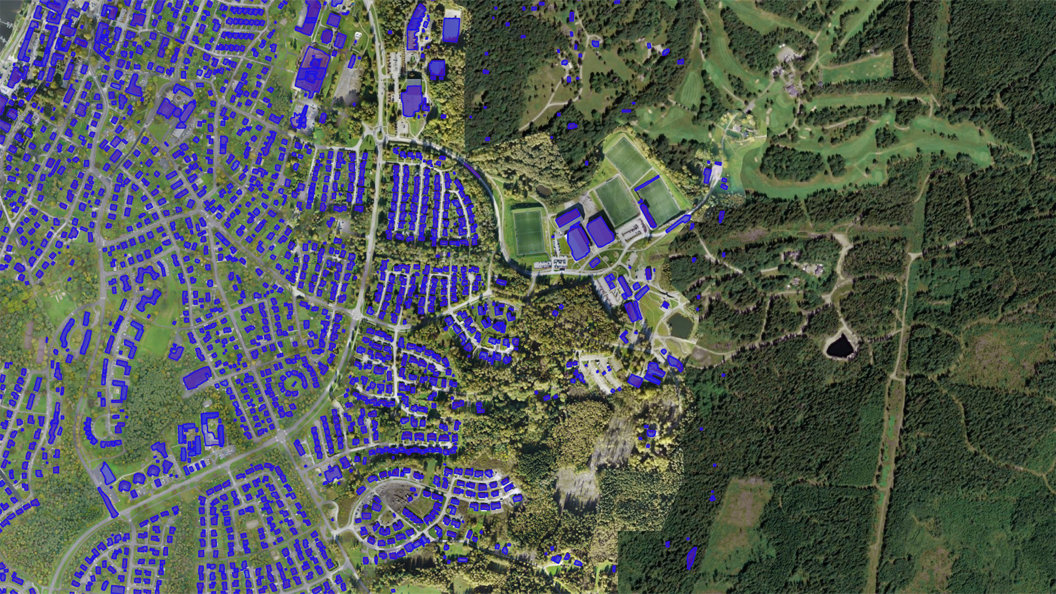 Luftbilddaten eines Vorortgebiets mit einem dichten Wald auf der rechten Seite. Die Dächer sind blau hervorgehoben und zeigen das Potenzial für die Installation von Solarkollektoren an.