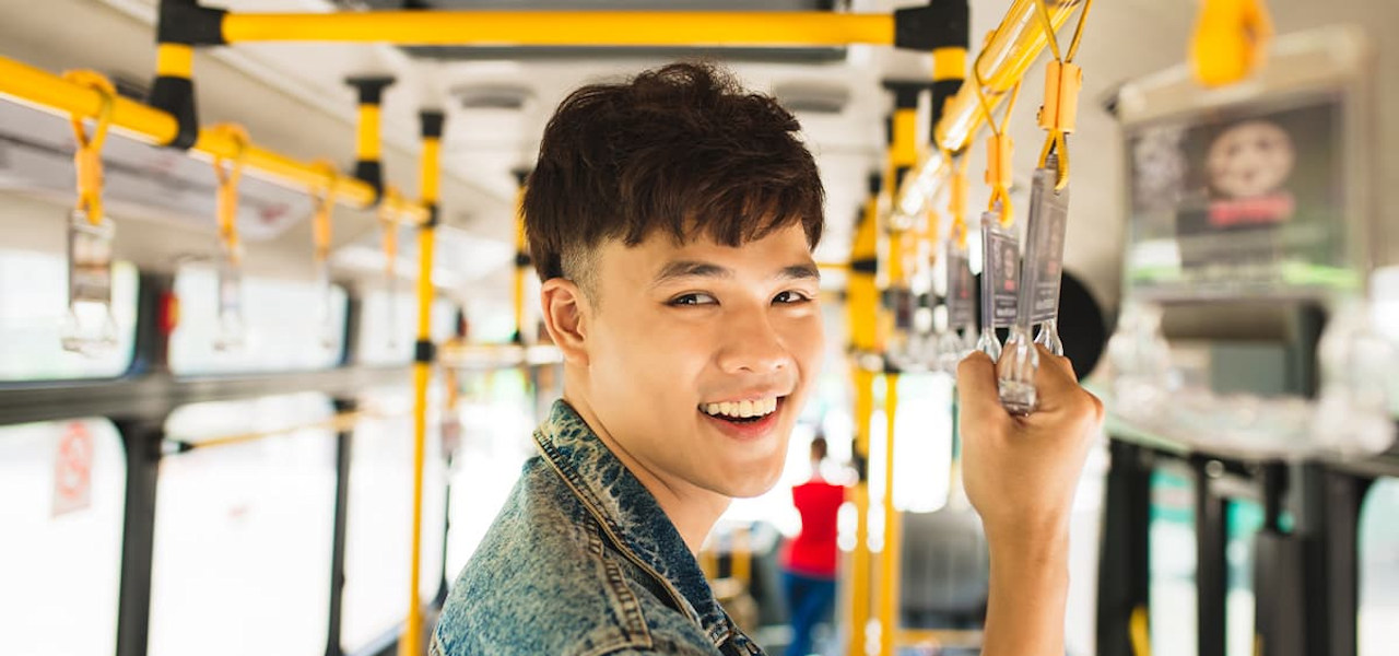 A happy young adult taking public transportation, standing on a bus