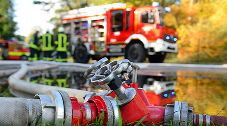 Feuerwehr-Einsatzauto mit Löschschläuchen und Feuerwehr-Mitarbeitenden im Hintergrund