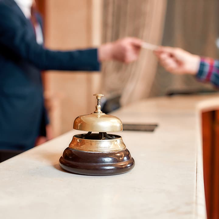 Gold bell on the registration counter in a hotel lobby and a guest handing their credit card to an employee in the background.