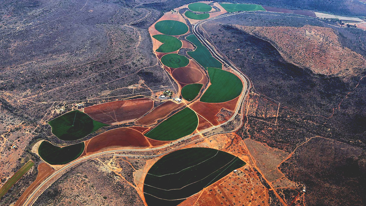 Off-nadr satellite imagery shows a swath of circular and semicircular fields winding through a dry region between plateaus