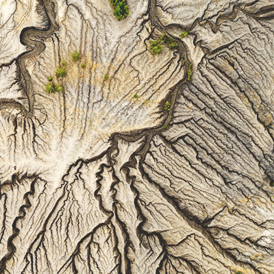 An aerial view of an abandoned quarry shows dry, dark brown water tracks through the light gray stone 