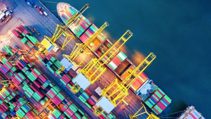 Luftaufnahme eines Frachtschiffes, das in blauem Wasser liegt und mit Frachtcontainern beladen wird